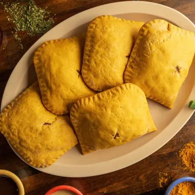 Five golden Jamaican beef patties on a white oval plate.