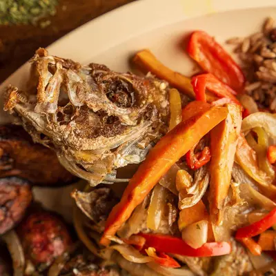 Escovitch whole fish topped with sauteed onions, red and orange peppers, with fried plantains alongside.