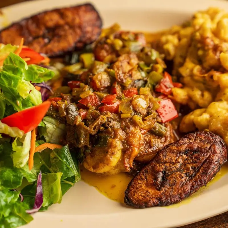 Curry shrimp with cabbage, salad and fried plantains on a white plate.