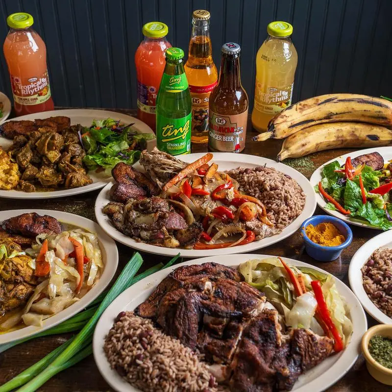 A table of Jamaican plates and bottled drinks photographed from above.