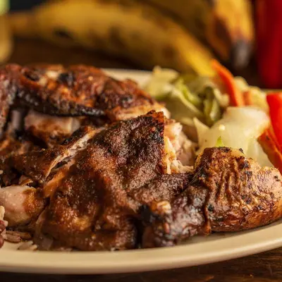 Grilled jerk chicken pieces close up, with cabbage and ripe plantains behind.