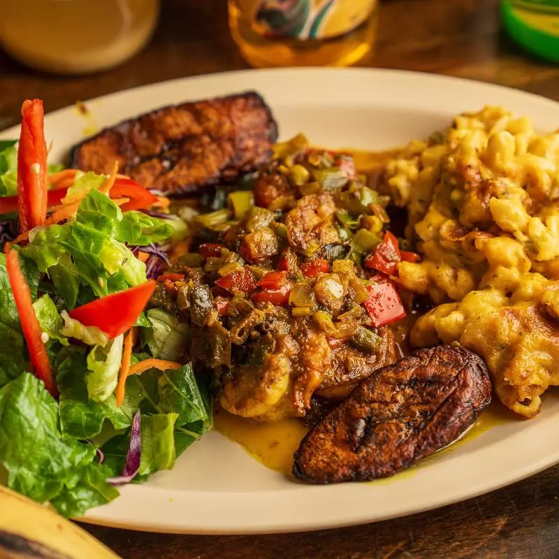 Jerk chicken with salad, plantains and jalapeno mac and cheese on a white plate.