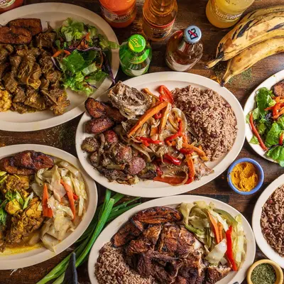Plates of curry goat, jerk chicken and rice and peas photographed together from above.