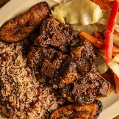 Brown stew chicken with rice and peas, cabbage and fried plantains.