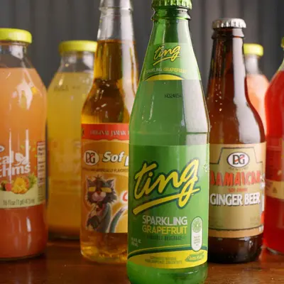 Bottles of Ting, D&G ginger beer and Tropical Rhythm juices lined up on a wooden table.