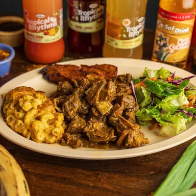 Curry goat served with sides of jalapeno mac and cheese, toss salad, and plantains.